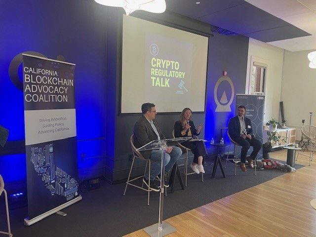 The Crypto Regulatory Talk fireside chat in progress, three speakers seated on stage beside a California Blockchain Advocacy Coalition banner